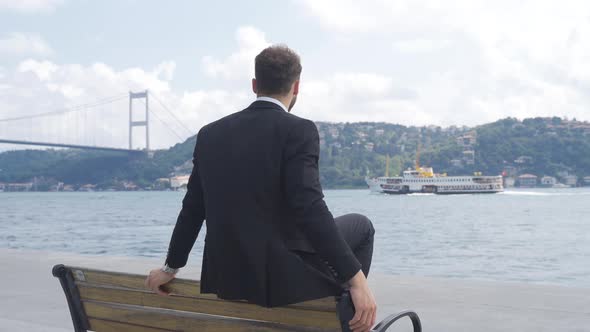 Thoughtful businessman watching the ship passing through the strait.