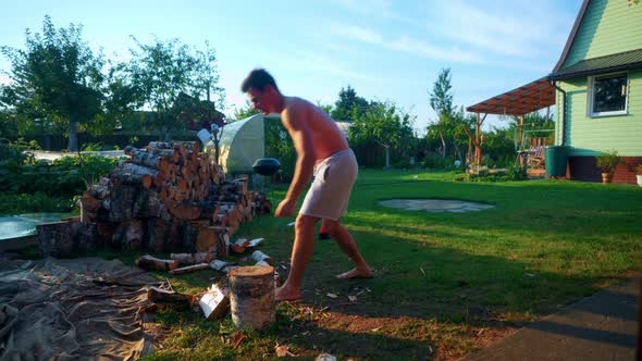 Shirtless Man Cutting Wood Logs With Hand Axe In The Backyard On A Sunny Summer Day. wide