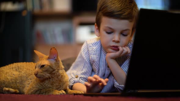 Funny Child with Kitten Using a Laptop at Home.