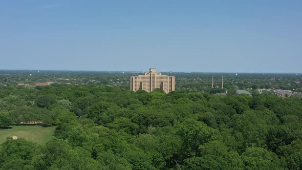 An aerial view over a large park with green trees. The drone camera dolly in and tilt down towards a