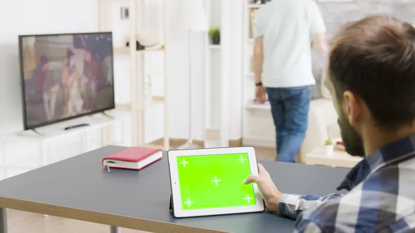 Man Scrolling on Digital Tablet PC with Green Screen in Bright Living Room