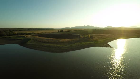 Flying Up Over Dam And Golden Fields At Sunset