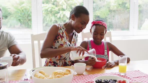 African american mother pouring milk in daughter's cereal bowl at home