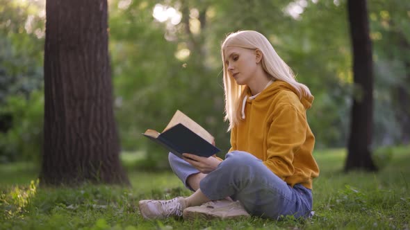 A Romantic Young Woman Reads a Fascinating Book with Interest in the Park on the Green Grass