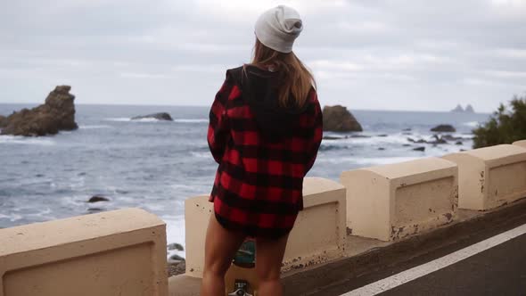 Stylish Sporty Builded Woman in Hat Long Plaid Coat and White Sneakers Enjoying Time By the Seaside