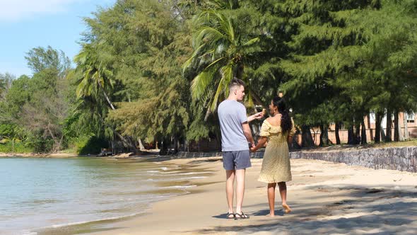 Romantic Interracial Couple Holding Hands and Walking on Beach on a Sunny Day