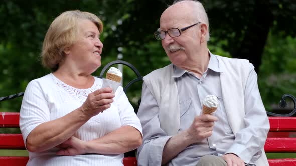 Mature couple sitting on a park bench and eating ice cream on a sunny day