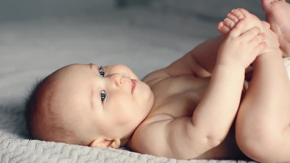 Adorable Smiling Caucasian 6 Months Old Baby Boy Holding His Feets and Looking at Camera While Lying