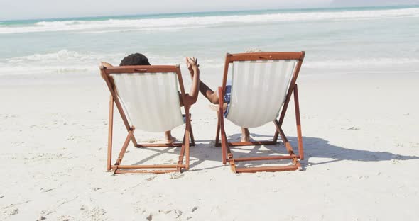 African american couple holding hands and lying on sunbeds on sunny beach