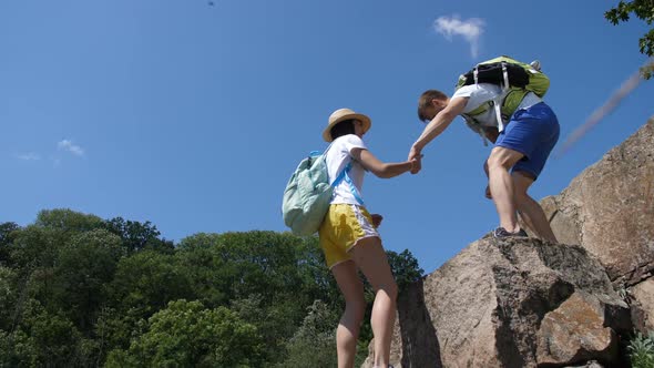 Hiking Man Helping Woman To Climb Up Steep Rocks