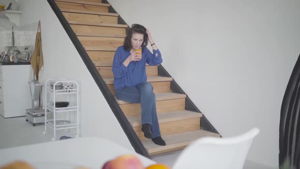 Wide Shot of Elegant Caucasian Brunette Woman Drinking Orange Juice in the Morning at Home. Portrait