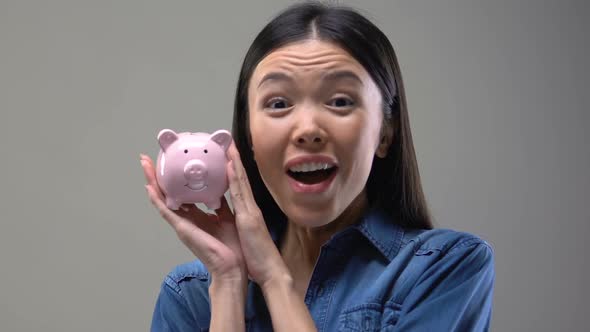 Smiling Asian Lady Shaking Piggy Bank, Money Saving Tips, Finance and Budget