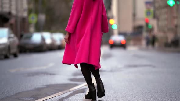 A Fashionable Woman with Black Hair, a Black Hat and a Purple Coat Walks Confidently on a Street in