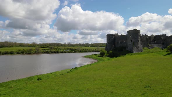 Carew Castle on verdant river shores, Wales. Aerial rising