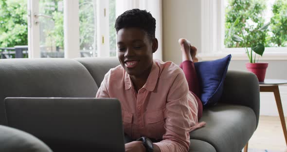 African american woman using laptop while lying on the couch at home