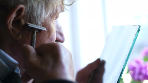 An Elderly Man Shaves His Face in Front of a Mirror