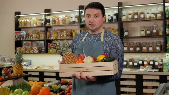 Portrait of a Male Salesman in an Apron with a Box of Fresh Fruit in His Hands