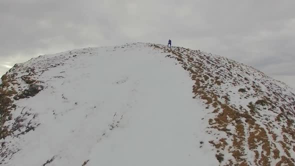 Aerial view of a trail runner running to the top of a snowy mountain