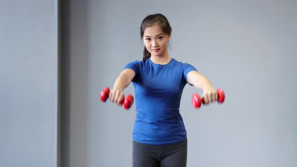 Medium Long Shot Smiling Asian Sports Woman Doing Exercise Lifting Dumbbells in Front of Herself