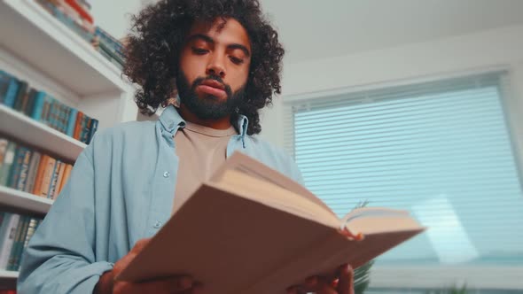 Young Carried Away Arabian Man Student Reading Book Stands in Library