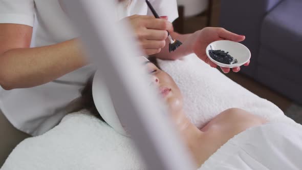 Caucasian woman lying back while beautician gives her a face mask