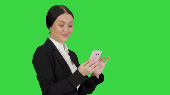 Smiling Businesswoman Checking Photos on Her Phone on a Green Screen, Chroma Key.