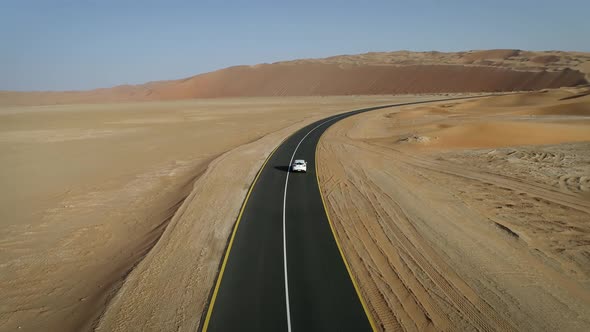 Aerial view of white car in clean road in the desert, Abu Dhabi, UAE.