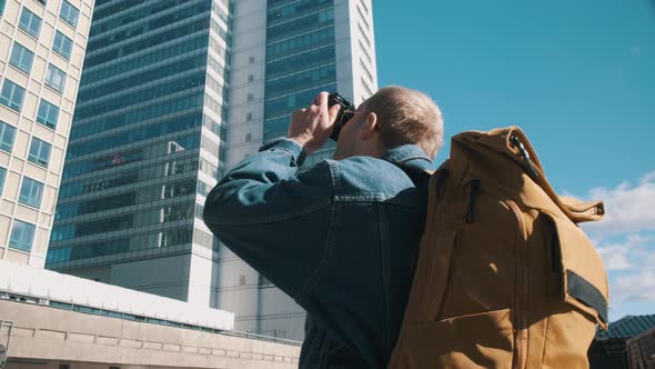 A Male Traveler with a Yellow Backpack Takes Pictures of the City on Camera