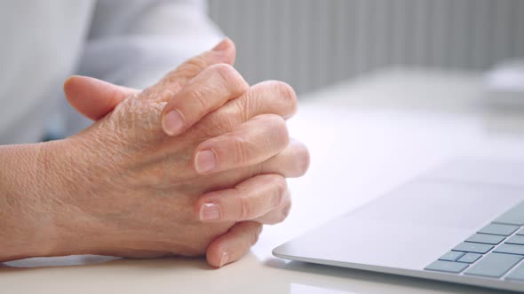 Senior woman worker puts folded overworked wrinkly hands on white table