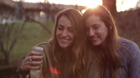 Sun setting behind twin teenage girls looking at cell phone