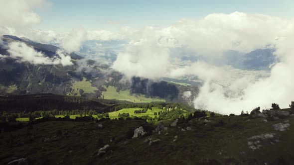 Aerial drone shot of a grass covered mountain top with a small trail leading up with clouds around.