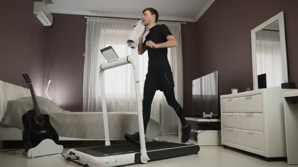 Man is wiping his face with towel during running on treadmill