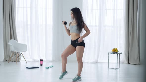 Wide Shot of Slim Charming Middle Eastern Woman Lifting Dumbbell in Hand Turning to Camera Smiling