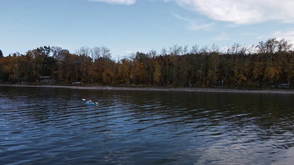 Drone footage of a caucasian woman paddling a blue kayak over Buffalo lake on a cloudy autumn day. A