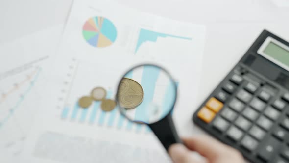 A Man are Calculating Expenses for a Month with Magnifier on Background of Calculator and Graphs