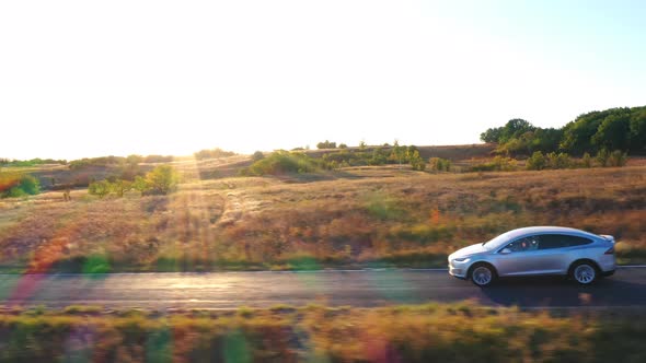 Aerial View of Electrical Car Speeding on Countryside Road with Beautiful Sunny Landscape at