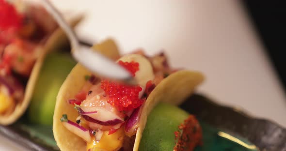 Chef In The Kitchen Putting Red Caviars On Top Of Sushi Tacos Using A Teaspoon. - close up shot