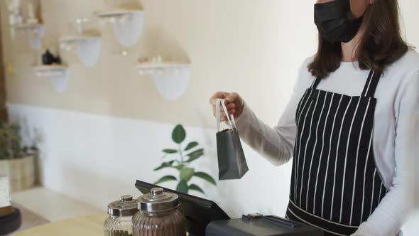 Caucasian waitress wearing face mask giving take-away order to caucasian female customer