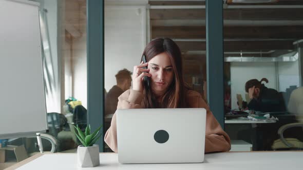 Young Busy Businesswoman at Her Desk Talking on the Phone and Looking at Computer of the Modern