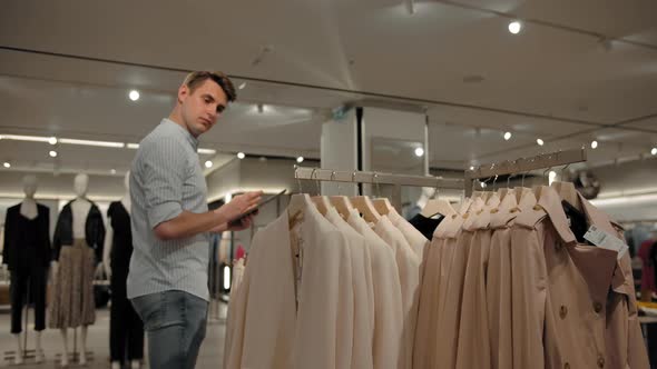 Male Examining and Supervising Clothes on Rails and Browsing Tablet Pc