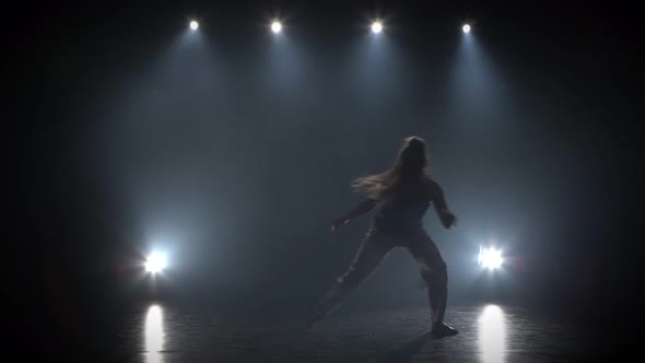 Woman with Long Hair Practicing Capoeira in Darkness Against Spotlight in Studio