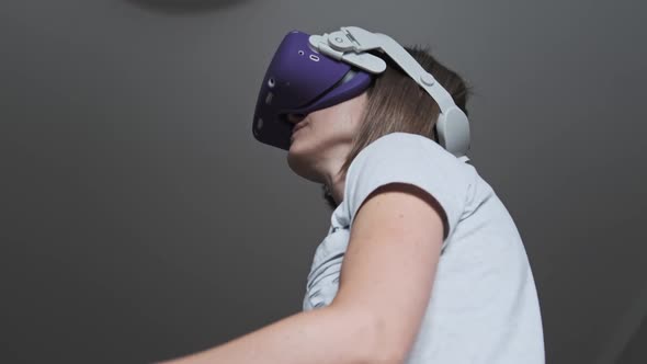 Young Woman in a Virtual Reality Headset Plays a Game at Home