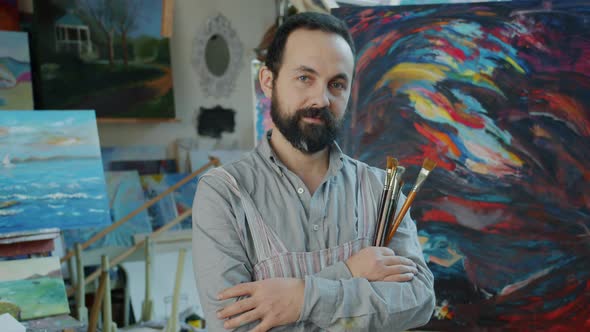 Portrait of Good-looking Man Artist Standing in Studio Holding Paintbrushes