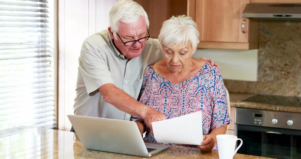 Senior couple calculating their bills on laptop in the kitchen