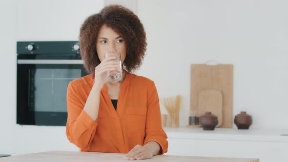 Thirsty African American Woman with Curly Hair Girl Drinking Water Standing in Kitchen in Morning