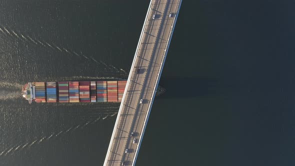 The Container Ship Passes Under a Large Bridge Over Which Cars are Moving