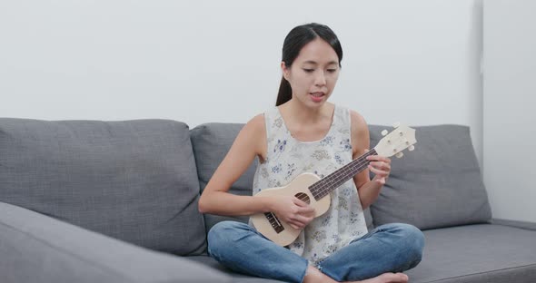 Woman play a song with ukulele at home