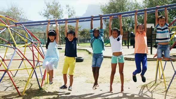 Happy schoolkids hanging on monkey bar