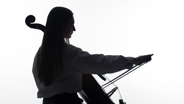 Silhouette of girl sitting and playing the cello on white background, side view. Studio shooting.