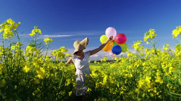 Woman walking with colorful balloons in mustard field